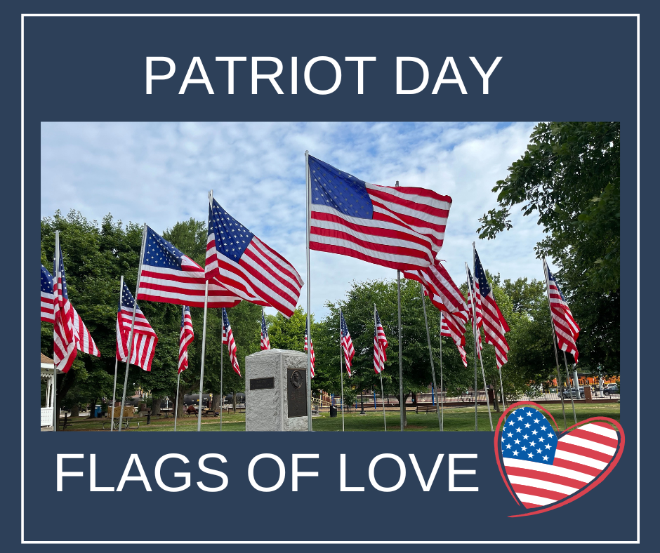 Several American flags on poles surround a memorial plaque in a park. The text reads Patriot Day Flags of Love with a heart-shaped American flag at the bottom right.